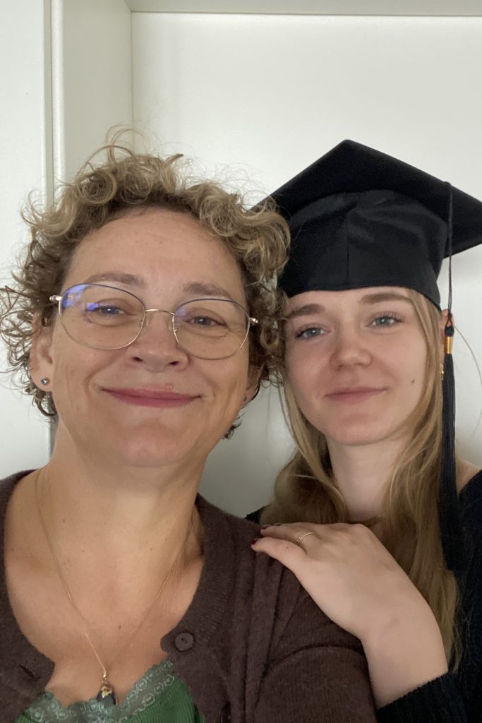 Zwei Frauen lächeln in die Kamera, eine trägt eine Abschlussmütze und legt die Hand auf die Schulter der anderen